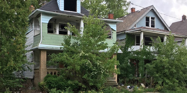 This Aug. 31, 2016, photo shows houses with missing windows and overgrown lawns along a street marred by cracks and potholes in East Cleveland, Ohio. Cleveland and East Cleveland, two of the country's poorest cities, are debating whether to merge, with both cities saying the state of Ohio needs to provide millions to begin fixing East Cleveland's infrastructure and finances.