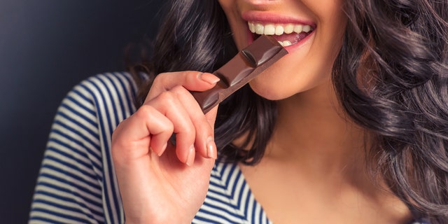 Cropped image of attractive girl eating chocolate and smiling, against dark background