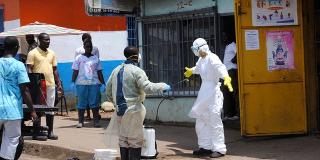A member of a burial team sprays a colleague with chlorine disinfectant in Monrovia October 20, 2014. The worst epidemic on record of the deadly virus Ebola has now killed more than 4,500 people in Liberia, Sierra Leone and Guinea. REUTERS/James Giahyue