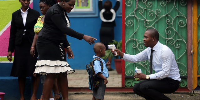 A school official takes a pupil's temperature using an infrared digital laser thermometer in front of the school premises, at the resumption of private schools, in Lagos in this September 22, 2014 file photo. REUTERS/Akintunde Akinleye
