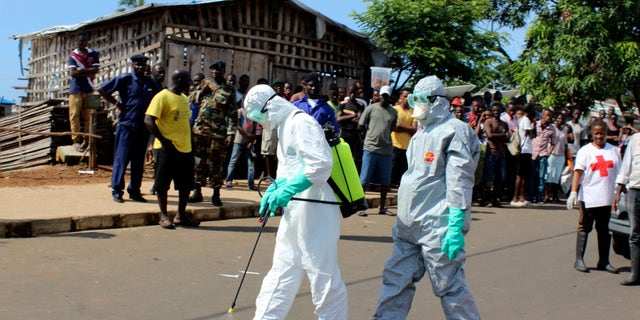 Health workers spray themselves with chlorine disinfectants after removing the body a woman who died of Ebola virus in the Aberdeen district of Freetown, Sierra Leone, October 14, 2014. REUTERS/Josephus Olu-Mammah