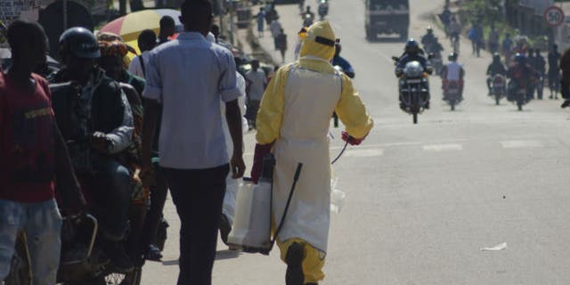 A health worker with disinfectant spray walks down a street outside the government hospital in Kenema, July 10, 2014. (REUTERS/TOMMY TRENCHARD)