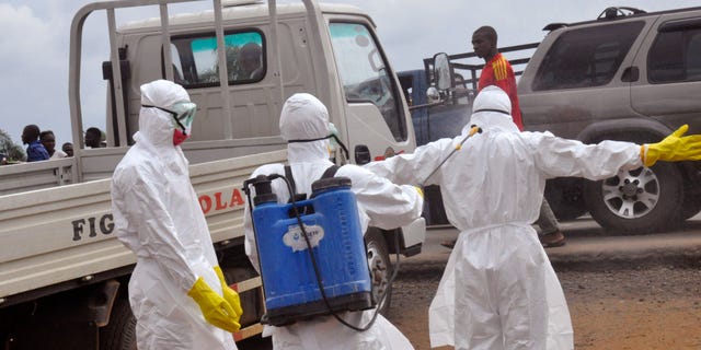 Health workers spray each other with disinfectant chemicals as they worked with a suspected Ebola virus death in Monrovia, Liberia, Thursday, Sept. 4, 2014. (AP Photo/Abbas Dulleh)