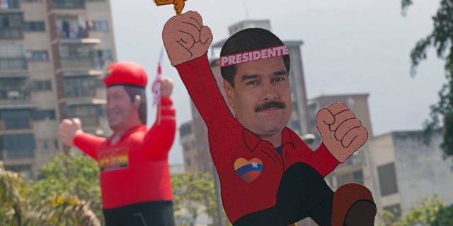A drawing of ruling party candidate Nicolas Maduro with a bird on his fist with an inflatable doll of the late Hugo Chavez in the background is held up as supporters move to the site of Maduro's closing campaign rally in Caracas, Venezuela, Thursday, April 11, 2013. Maduro, Chavez's hand-picked successor, assured last week during a campaign rally that Venezuela's late President Hugo Chavez's spirit appeared to him in the form of a little bird that flew around his head inside a wooden chapel to give him his blessing. He is running for president against opposition candidate Henrique Capriles in the presidential election set for Sunday, April 14. (AP Photo/Ramon Espinosa)