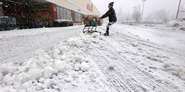 A woman fights to drag her shopping cart to her vehicle after exiting the Shaws Supermarket in Dartmouth, Mass., as a snowstorm swept across the area on Thursday.