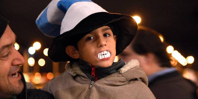 A child shows his support for Uruguay player Luis Suarez, by wearing toy plastic vampire's teeth, as he awaits the arrival of Suarez at Carrasco International Airport in the outskirts of Montevideo, Uruguay, Thursday, June 26, 2014. The Uruguay forward, widely regarded as one of the best players in the world, was banned by FIFA from all football for four months on Thursday for biting an Italian opponent in an incident that marred the team's victory and progression to the second round. (AP Photo/Matilde Campodonico)