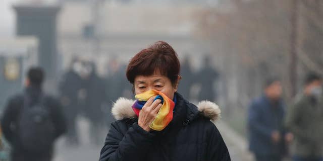 FILE - In this Tuesday, Dec. 20, 2016, file photo, a woman uses a scarf to cover her mouth for protection against the air pollution as she walks on a street in Beijing, China. Beijing will spend $2.7 billion to fight air pollution in the capital this year, state media reported Thursday. (AP Photo/Andy Wong, File)