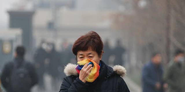 FILE - In this Tuesday, Dec. 20, 2016, file photo, a woman uses a scarf to cover her mouth for protection against the air pollution as she walks on a street in Beijing, China. Beijing will spend $2.7 billion to fight air pollution in the capital this year, state media reported Thursday. (AP Photo/Andy Wong, File)