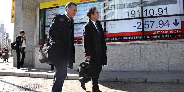 Men walk past an electronic stock indicator of a securities firm in Tokyo, Tuesday, Jan. 31, 2017. Asian shares slipped Tuesday, tracking a decline on Wall Street set off by jitters over President Donald Trump's travel ban. (AP Photo/Shizuo Kambayashi)