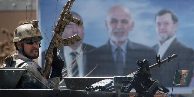 An Afghan special forces soldier takes up position next to an election campaign poster of presidential candidate Ashraf Ghani Ahmadzai, center on the poster, after the Taliban launched an assault with a suicide bomber detonating his vehicle outside an election office in Kabul, Afghanistan, Tuesday, March 25, 2014. Gunmen stormed into the building, trapping dozens of employees inside and killing many people. A candidate for a seat on a provincial council was among those killed, along with an election worker, a civilian and a policeman. (AP Photo/Anja Niedringhaus)