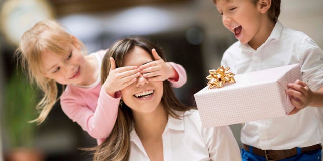 Happy kids surprising mom with a gift on mother's day