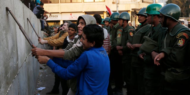 Dec. 9, 2012: Protesters break iron bars on cement blocks, as Egyptian army soldiers stand guard in front of the presidential palace in Cairo, Egypt.