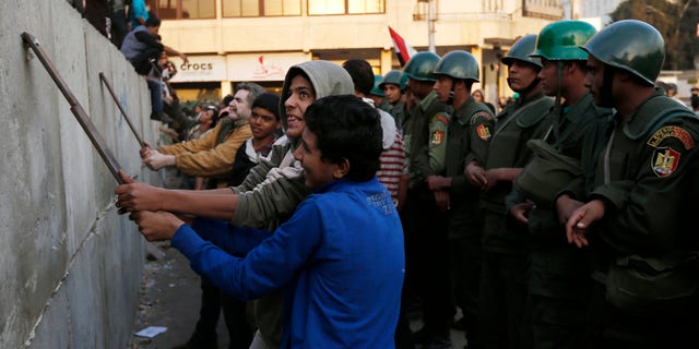 Dec. 9, 2012: Protesters break iron bars on cement blocks, as Egyptian army soldiers stand guard in front of the presidential palace in Cairo, Egypt.