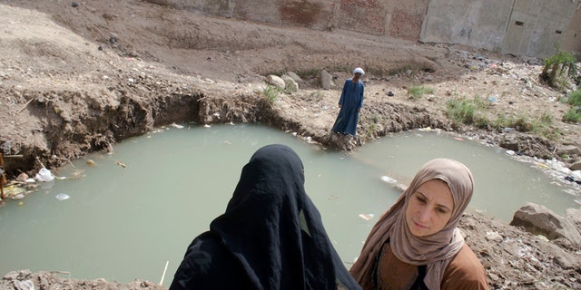 People gather near water which covered the site of a recently discovered statue in a Cairo slum that may be of pharaoh Ramses II, in Cairo, Egypt, Friday, March 10, 2017.