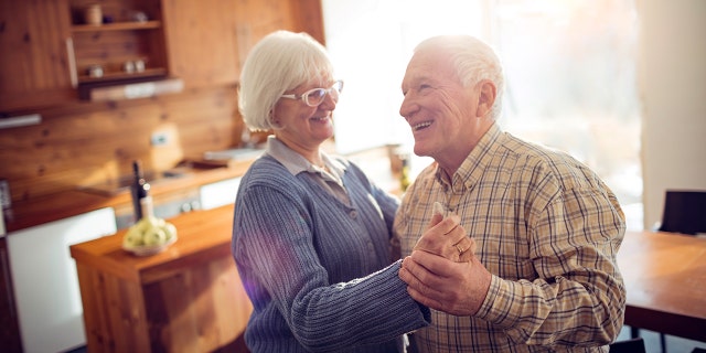 An elderly couple dance in their kitchen.