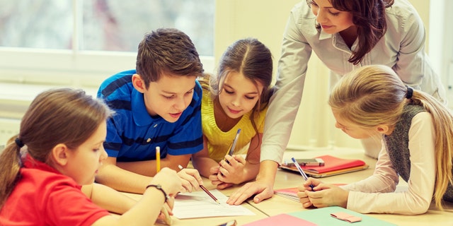 education, elementary school, learning and people concept - teacher helping school kids writing test in classroom