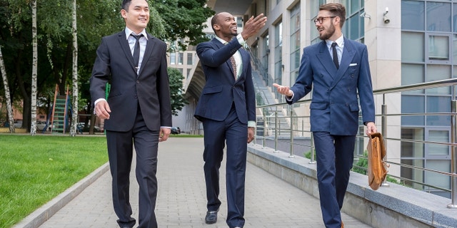 Portrait of multi ethnic business team.Three smiling men walking against the background of city. The one man is European, other is Chinese and African-American.