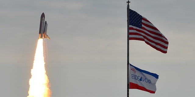 Space shuttle Endeavour appears to fly past flags in the foreground, on its way to the International Space Station. Launch of the STS-134 mission took place at 8:56 a.m. EDT on May 16.