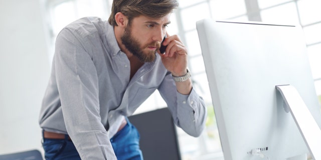 Shot of a designer talking on his phone while reading something on his computer screen