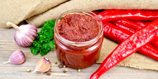 Tabasco in a glass jar, fresh red peppers, garlic, peppercorns, mustard seeds on the background burlap and wooden planks