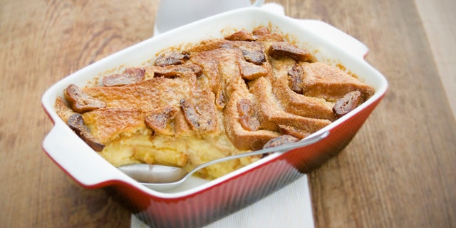 Traditional British Dessert, Bread and Butter Pudding with Custard. Served in a red oven dish on wood.