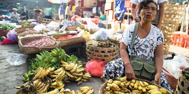 A vendor sells fruit in a bustling Balinese market.