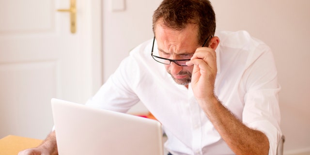 A businessman is shown sitting at his desk with his laptop. 