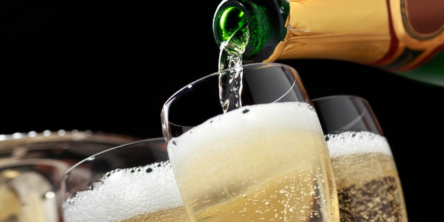 Champagne is being poured into several champagne glasses. The glasses sit in front of the ice bucket that held the champagne bottle as bubbles from the freshly poured champagne can be seen. The camera is tilted slightly of axis.