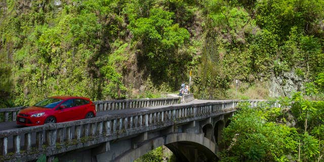 In this Sept. 24, 2014 photo, a car crosses a stone bridge on the Hana Highway in Hana, Hawaii. The road cuts through Mauis valleys and mountains and slithers above its coastal shores. The drive winds past long stretches of swaying sugar cane fields and blue ocean views with kite surfers soaring through the sky. The notorious curves dont appear until well into the drive when the fields and ocean give away to tropical flowers and jungle greens. (AP Photo/Marco Garcia)