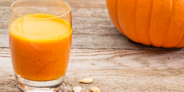 a glass of fresh pumpkin juice on a rustic wooden table with pumpkin and seeds