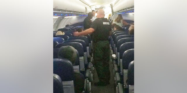 This Tuesday, Nov. 3, 2015, photo provided shows airport police aboard a plane after an emergency landing at Eisenhower National Airport in Wichita, Kan. The U.S. Attorney's Office says a disruptive passenger who forced the diversion of the American Airlines flight from Phoenix to New York will face federal charges.