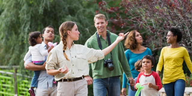Multi-ethnic tourists with young children (3 to 7 years) visiting a park, walking with tour guide. Focus on guide.