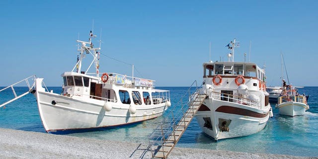 Greece, Skiathos, tourists boats with gangways moored on Lalaria beach at water's edge set against clear blue sky