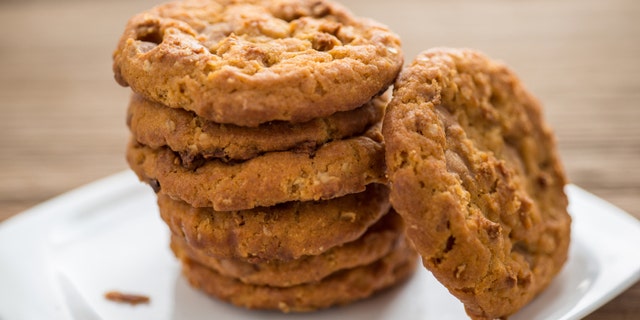 Stacked chocolate chip cookies and white plate on wooden table