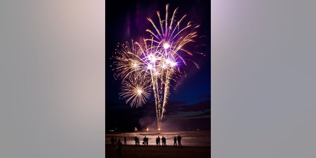 Spectators standing on the beach and looking at fireworks