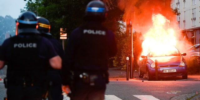 Police officers watch a car burning in Nantes.