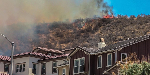 In this July 9, 2016 photo, flames line a hillside behind homes on Old Stone Way as the Sage Fire roared through the Stevenson Ranch area of Santa Clarita, Calif. A fast-moving brush fire north of Los Angeles has sent about 2,000 people fleeing from their homes.  (Austin Dave/The Santa Clarita Valley Signal via AP)