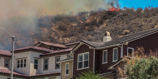 In this July 9, 2016 photo, flames line a hillside behind homes on Old Stone Way as the Sage Fire roared through the Stevenson Ranch area of Santa Clarita, Calif. A fast-moving brush fire north of Los Angeles has sent about 2,000 people fleeing from their homes. (Austin Dave/The Santa Clarita Valley Signal via AP)