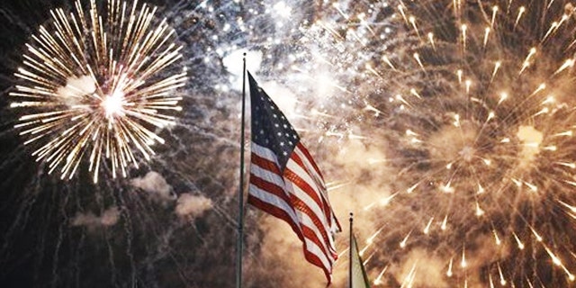 Fireworks explode behind the US flag at the July 4th celebration at State Fair Meadows in East Rutherford, NJ.