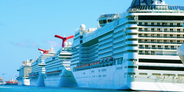 Row of big huge cruise ships lined up docked in a port with beautiful aqua colored water.