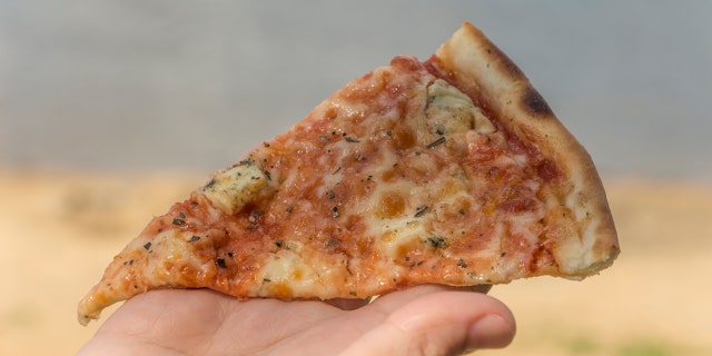 Fast food, female hand holding a slice of pizza, on the beach.