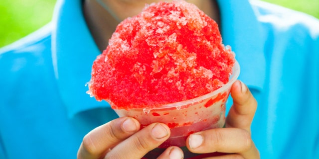 A young African-American boy holds a snow cone as he smiles at the camera.