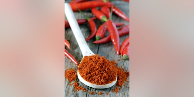 close up of spoon heaped with chilli powder with red chillies in background