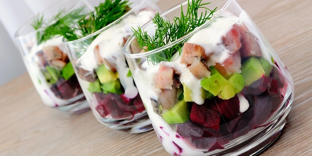 Beetroot salad with avocado and herring in cream sauce in a glass