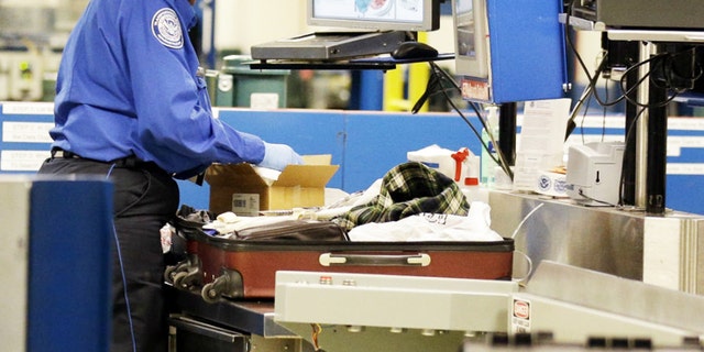 A TSA agent inspects a package inside a suitcase.