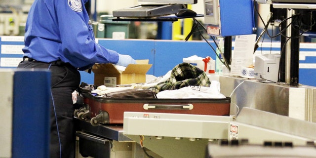 A TSA agent inspects a package inside a suitcase.