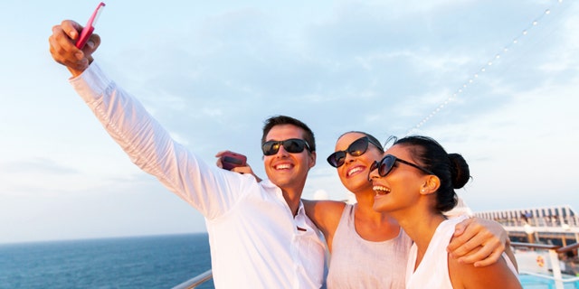 group of friends taking self portrait using smart phone on cruise