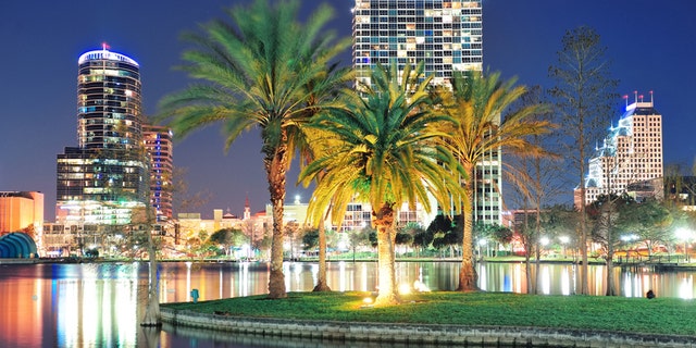 Orlando downtown skyline panorama over Lake Eola at night with urban skyscrapers, tropic palm tree and clear sky.