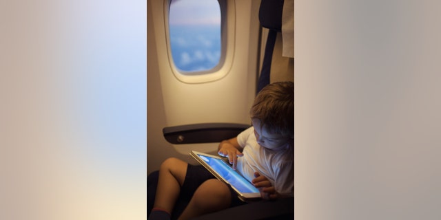 Little boy in the plane sitting by the illuminator and using touch pad to entertain himself