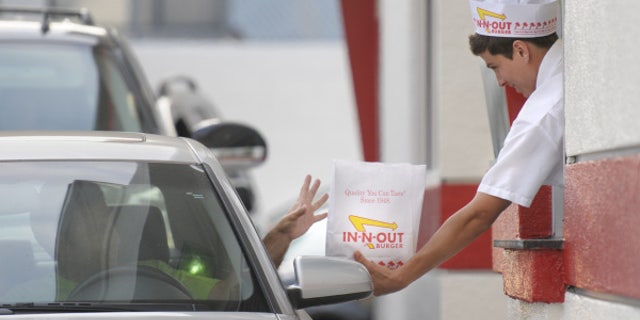 In this June 11, 2010 photo, a customer reaches for his order from the drive-through at In-N-Out Burger in the Hollywood area of Los Angeles. Amid complaints of obesity and lines of idled cars stretching into neighborhood streets, this blue-collar town is banning new drive-throughs in hopes of shedding its reputation as a haven for convenient, fatty foods. (AP Photo/Adam Lau)